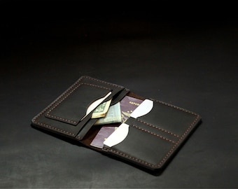 May include: Open, dark brown leather wallet with visible stitching. The wallet contains cash, a passport, and white card inserts. The interior is a lighter brown. The wallet is open and displayed against a dark background.