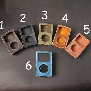 May include: Six leather cases for portable media players arranged in an arc. Cases 1 through 5 are empty, featuring stitched edges and cutouts for screens and click wheels. Case 6 is blue, contains a black media player, and is labeled with a 6.