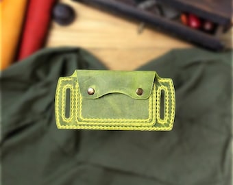 May include: A handcrafted, olive green leather wallet with yellow stitching. The wallet features a flap closure secured by two brass-colored rivets. The edges are meticulously stitched with bright yellow thread, adding a contrasting detail to the design. The wallet is a stylish accessory.