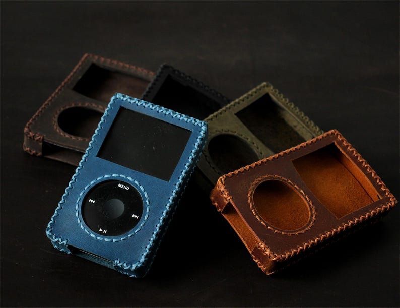 May include: A collection of rectangular leather cases for portable media players, featuring hand-stitched edges. The cases are available in blue, dark brown, black, and olive green, each with a cutout for the screen and circular click wheel.