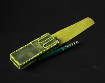 May include: A rectangular olive green leather pen case with a lime green stitched edge and a matching lime green flap, accompanied by a teal fountain pen featuring a gold-colored clip and a thin gold band around the center of the barrel.
