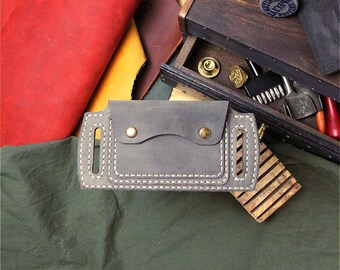 May include: A rectangular grey leather belt pouch featuring a flap closure secured by two brass-coloured metal snaps. The pouch has two vertical belt loops on the sides and is constructed with visible thick white stitching along the edges.