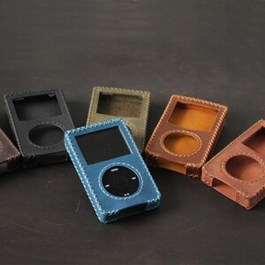 May include: A collection of six rectangular leather cases for portable media players, each featuring a circular cutout for a click wheel and a square cutout for a screen. The cases are available in blue, black, olive green, and various shades of brown.