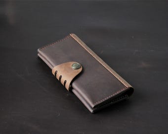May include: A dark brown leather wallet with a light brown accent and a metal button closure. The wallet is rectangular and appears to be closed. The stitching is visible along the edges, and the leather has a textured appearance.