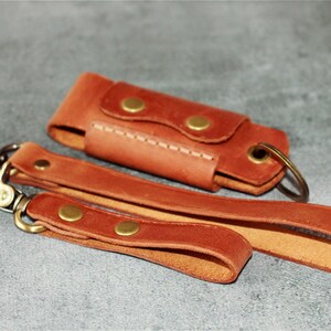 May include: A set of three brown leather accessories: a key fob, a wrist strap, and a small case. The key fob and wrist strap have brass-colored clasps and rivets. The case has a snap closure and a key ring.