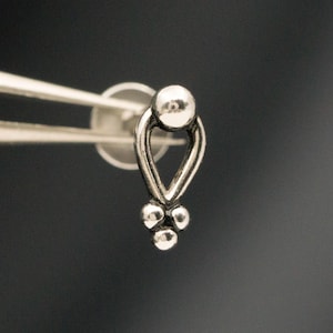 May include: A silver-toned stud earring featuring a teardrop-shaped frame with a small sphere at the top and a cluster of three tiny spheres at the bottom point. The metal piece is held by tweezers and includes the text Type A in the corner.