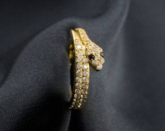 May include: A gold snake ring with a black stone for an eye, set with clear stones around the body of the snake.