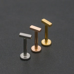 May include: Three barbell earrings with different coloured tops. The tops are silver, rose gold, and gold. The earrings are all the same size and shape.
