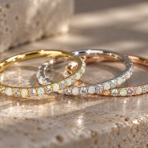 May include: Three thin metal rings arranged in a row, each featuring a continuous band of small, round, iridescent opal stones. The rings are crafted in yellow gold, silver, and rose gold tones, showcasing a delicate and uniform circular design.