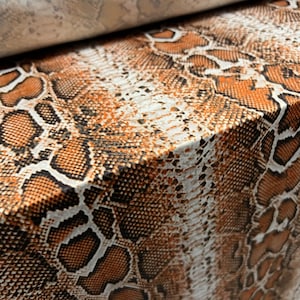 Könnte beinhalten: Nahaufnahme eines braunen und weißen Schlangenlederstoffs mit einem strukturierten Muster.