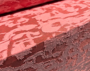 May include: Close-up of a pink fabric with a textured, embossed pattern. The fabric has a subtle sheen and a slightly rough texture.