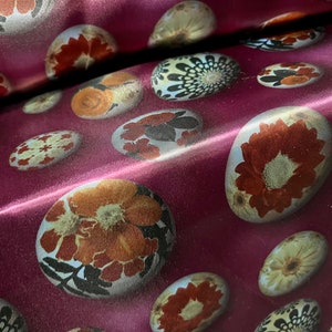 May include: A close-up of a burgundy fabric with a repeating pattern of white circles with floral designs in shades of brown, orange, and black.
