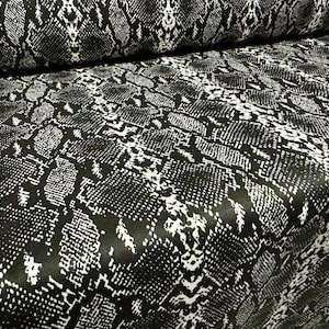Peut inclure: Tissu à motif peau de serpent noir et blanc. Le tissu a un léger brillant et une surface texturée.