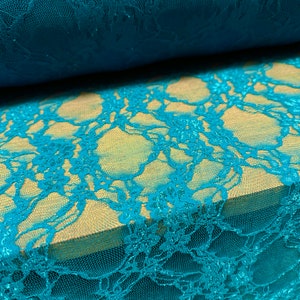 May include: Teal lace fabric with a delicate floral pattern. The lace is soft and sheer, with a subtle shimmer.
