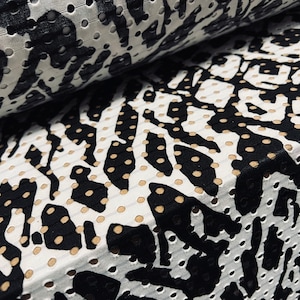 May include: Close-up of a perforated fabric with a black and white animal print design. The fabric is layered, showing the texture and pattern. The design features irregular black shapes on a white background, with small, evenly spaced holes.