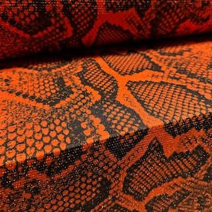 May include: Close-up of orange and black fabric with a snakeskin pattern. The fabric has a subtle shimmer.