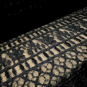 Pu&ograve; includere: Tessuto di pizzo nero con un motivo dorato. Il pizzo ha un design delicato e intricato.