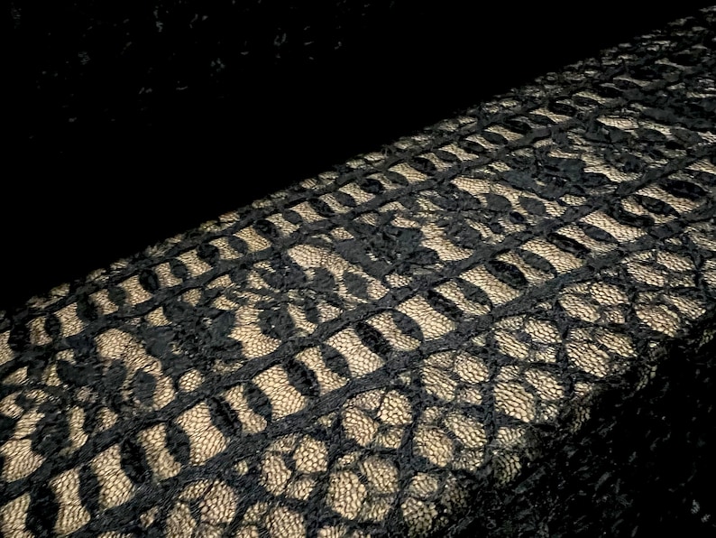 Pu&ograve; includere: Tessuto di pizzo nero con un motivo dorato. Il pizzo ha un design delicato e intricato.