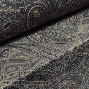 May include: Close-up of a fabric with a detailed paisley pattern. The design features swirling, teardrop-shaped motifs in shades of gray, black, and beige. The fabric appears to be folded, revealing the intricate pattern.
