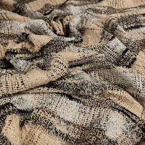 Könnte beinhalten: Nahaufnahme eines beige-schwarz-weißen Strickstoffes mit einer strukturierten, offenen Webart. Der Stoff hat ein gestreiftes Muster.