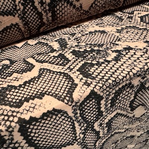 May include: Close-up of a fabric with a black and beige snake skin pattern.