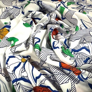May include: White fabric with a floral print featuring blue, green, orange, and red flowers. The flowers are outlined in black and the background has thin black stripes.