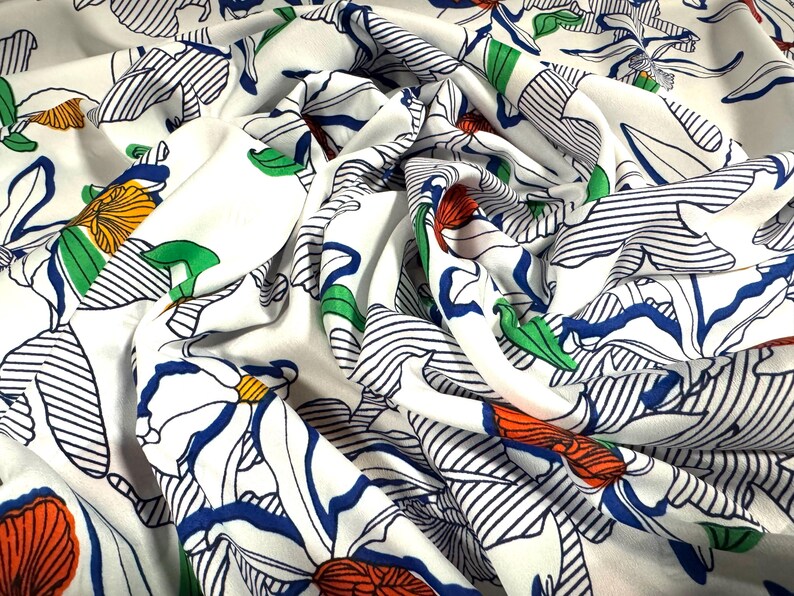 May include: White fabric with a floral print featuring blue, green, orange, and red flowers. The flowers are outlined in black and the background has thin black stripes.