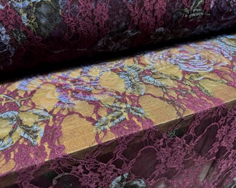 May include: Close-up of a fabric roll featuring a floral design. The fabric has a burgundy lace overlay, with a yellow and floral pattern underneath. The floral pattern includes roses and leaves in shades of blue, yellow, and pink.
