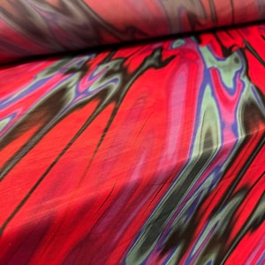 Könnte beinhalten: Leuchtend roter Stoff mit einem fließenden, abstrakten Muster. Das Design enthält Streifen in Schwarz, Blau und Grün, wodurch ein dynamischer und farbenfroher visueller Effekt entsteht. Geeignet für Kleidung oder Heimtextilien.