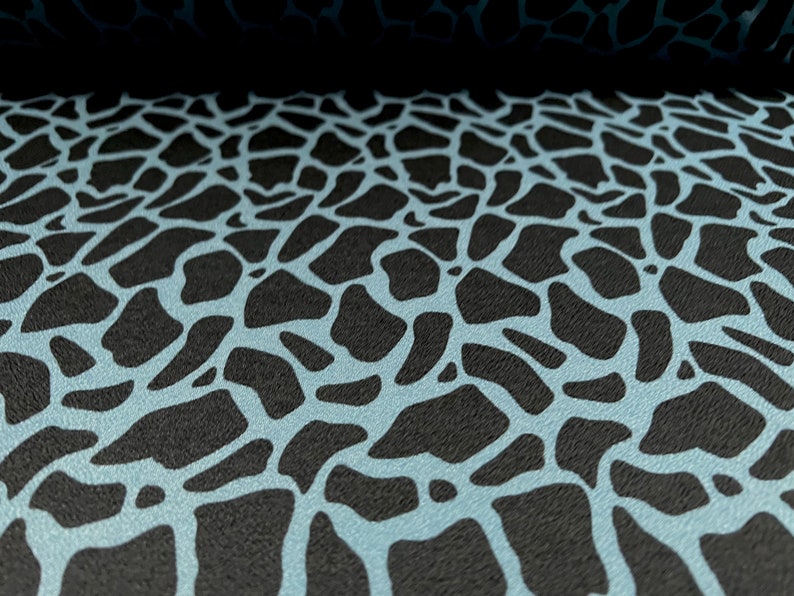 May include: A close-up of a black and light blue fabric with a repeating pattern of irregular shapes. The fabric has a textured surface.