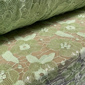 May include: Pale green floral lace fabric with sequins. The lace features a delicate floral pattern with small sequins scattered throughout.