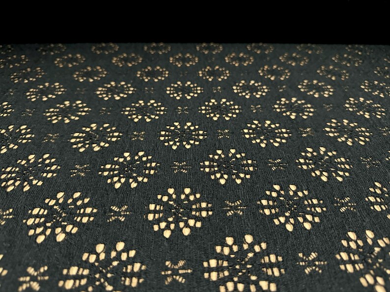 May include: Black fabric with a repeating pattern of small, beige, floral shapes.