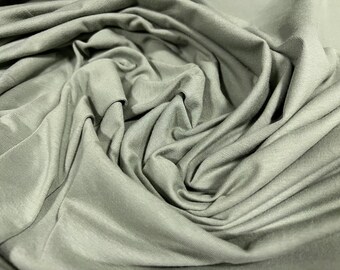May include: A close-up of a soft, smooth, sage green fabric. The fabric is draped and folded, creating a textured, abstract pattern.
