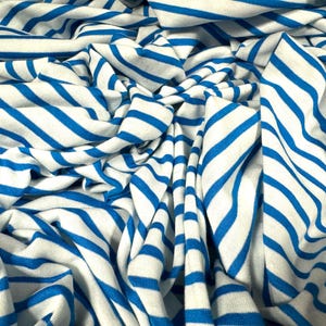 Op de afbeelding: Witte en blauwe gestreepte stof met een zacht, gestructureerd gevoel. De stof is gevouwen en gekreukt, waardoor een dynamisch patroon ontstaat.