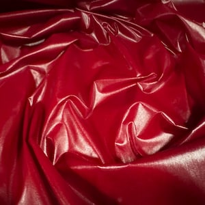 May include: Close-up of a deep red fabric with a shiny, satin-like finish. The fabric is draped and folded, creating soft, flowing curves.