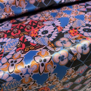May include: A close-up of a fabric with a colorful floral pattern. The fabric is a mix of blue, pink, orange, and black. The pattern is made up of flowers, leaves, and geometric shapes.