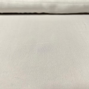 May include: A close-up of a white fabric with a subtle textured pattern. The fabric is smooth and appears to be soft.