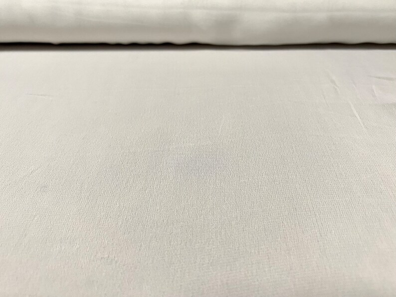 May include: A close-up of a white fabric with a subtle textured pattern. The fabric is smooth and appears to be soft.