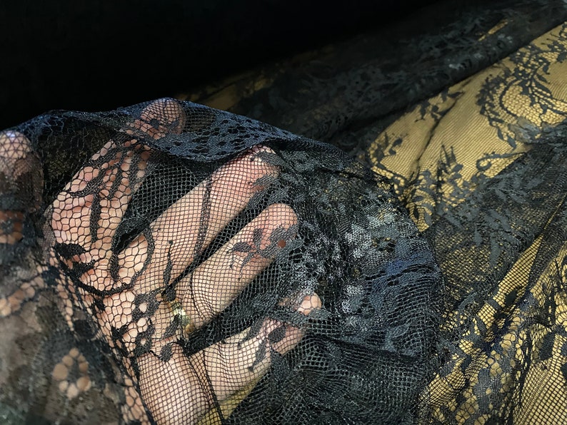 May include: Black lace fabric with a delicate floral pattern. The lace is soft and sheer, and it has a slightly textured surface.