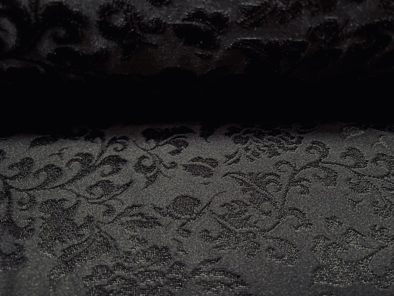 May include: Black fabric with a raised floral pattern. The fabric has a subtle sheen and a soft texture.