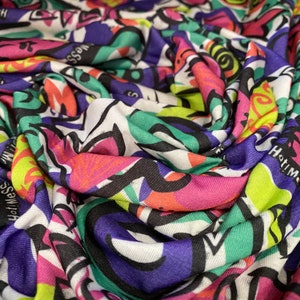 May include: A colorful fabric with a repeating pattern of black, white, green, pink, purple, and yellow abstract shapes and the words "Hatim" and "Haf Messe".