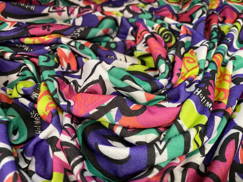 May include: A colorful fabric with a repeating pattern of black, white, green, pink, purple, and yellow abstract shapes and the words "Hatim" and "Haf Messe".