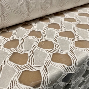 May include: White lace fabric with a geometric pattern. The lace is sheer and has a delicate, intricate design.
