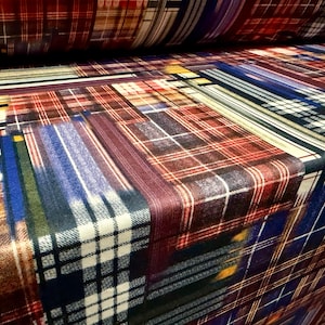 May include: A close-up of a fabric roll displaying a patchwork design of diverse plaid patterns. The fabric incorporates a variety of colours, such as red, blue, brown, and white, resulting in a visually striking textile.
