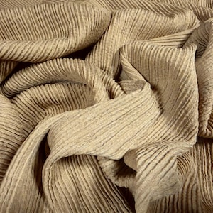 May include: Close-up of a beige fabric with a ribbed texture. The fabric is draped and folded, creating shadows and highlights. The material appears soft and flowing, with a subtle sheen. The overall effect is one of luxury and comfort.