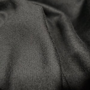 Pode incluir: Close-up de um tecido preto com uma superfície texturizada. O tecido é macio e tem um brilho sutil.