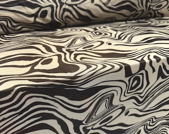 May include: Close-up of a fabric with a zebra stripe pattern. The fabric is a cream color with black stripes that curve and swirl across the surface. The fabric is folded over in the upper left corner.