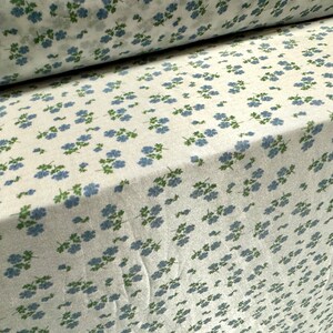 May include: White fabric with a repeating pattern of small blue flowers with green stems.