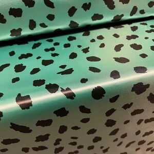 May include: Teal fabric with a black leopard print pattern. The fabric has a satin finish.
