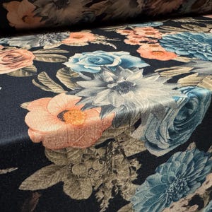May include: Close-up of a fabric with a dark blue background and a floral pattern. The flowers are in shades of peach, light blue, and white, with green and brown leaves. The fabric has a soft, textured appearance.